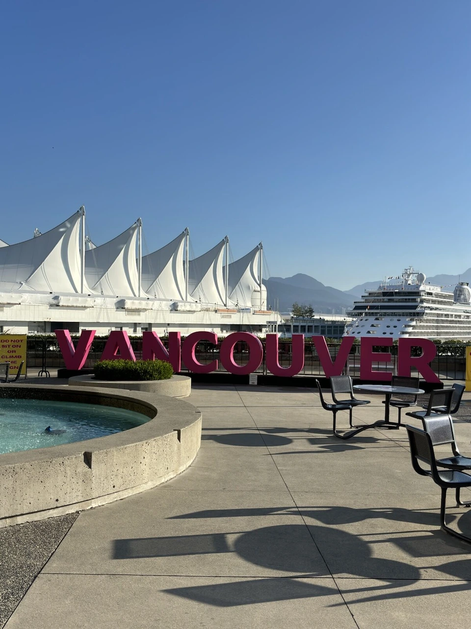 バンクーバーのカナダプレイスの白い帆の屋根とピンクのVANCOUVERの文字、奥に停泊中のクルーズ船