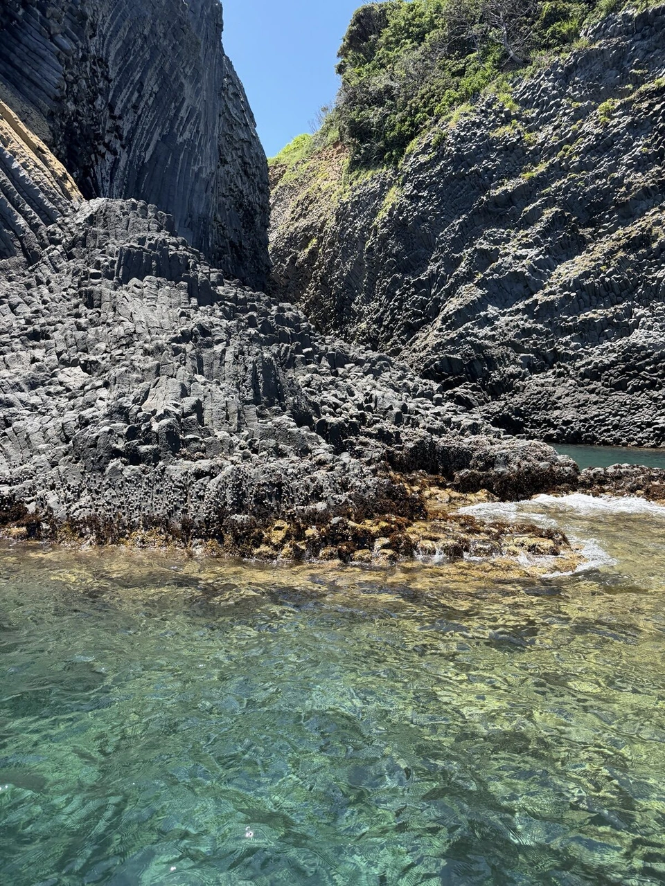 七ツ釜の柱状節理の岩が積み重なった崖と、手前の透明な海