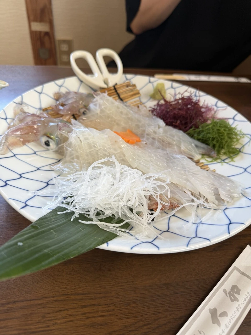 唐津市鎮西町の「大和」のイカの活き造り。網目模様の大皿に透明な身と大根のつま、海藻、ハサミ