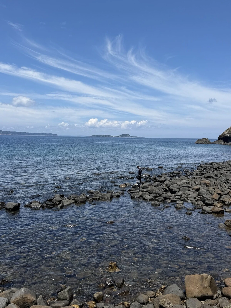 沖へ向かって岩が点々と続く磯。遠くに島が見え、空には筋状の雲
