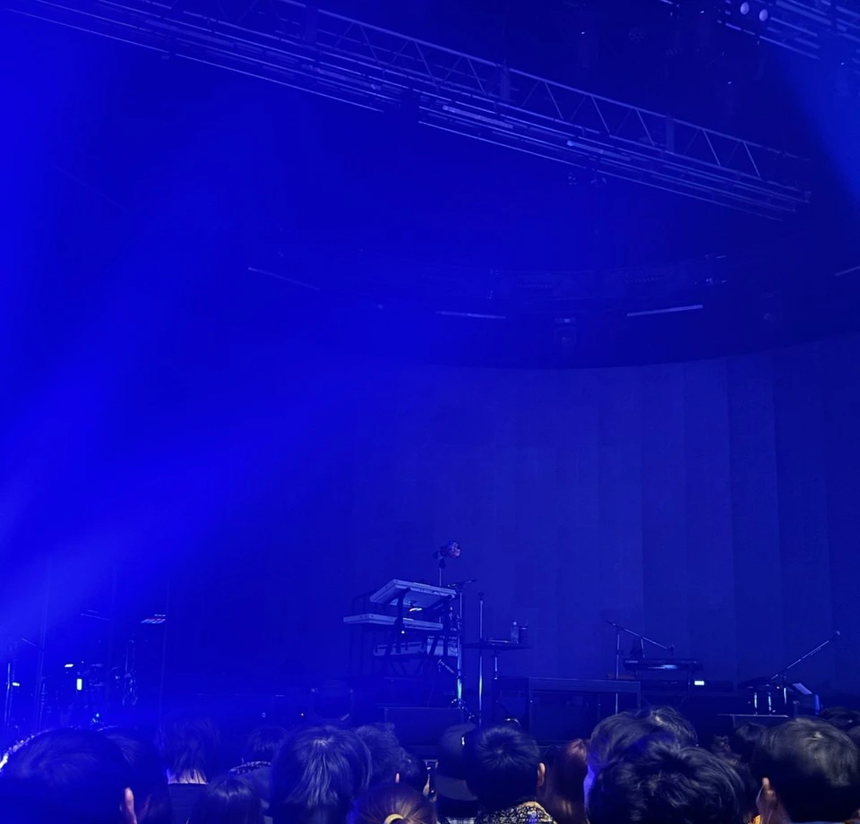 開演前のZepp Osaka Baysideの場内。青い照明の中に楽器が並ぶステージ、手前に立って待つ観客の頭