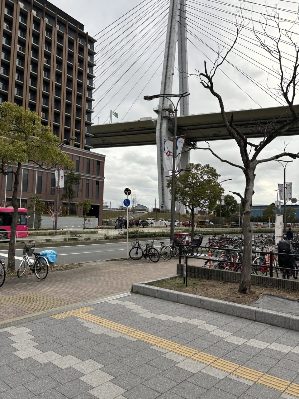 桜島駅から会場へ向かう歩道。左に高い建物、右奥に大きな橋の柱と高架の道路、手前の植え込みの横に自転車
