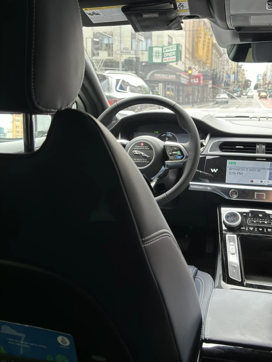 Waymoの後部座席から見た車内。誰も座っていない運転席とハンドル、画面に到着まで2分の表示、窓の外にパウエル通りの街並み