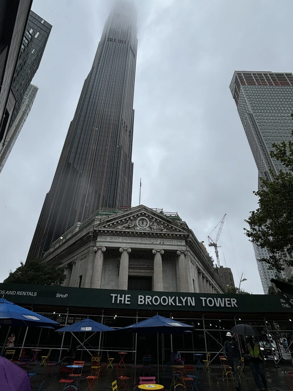 雨の日に足元から見上げたブルックリン・タワー。上のほうは霧に隠れ、手前に古い銀行の建物とTHE BROOKLYN TOWERの看板