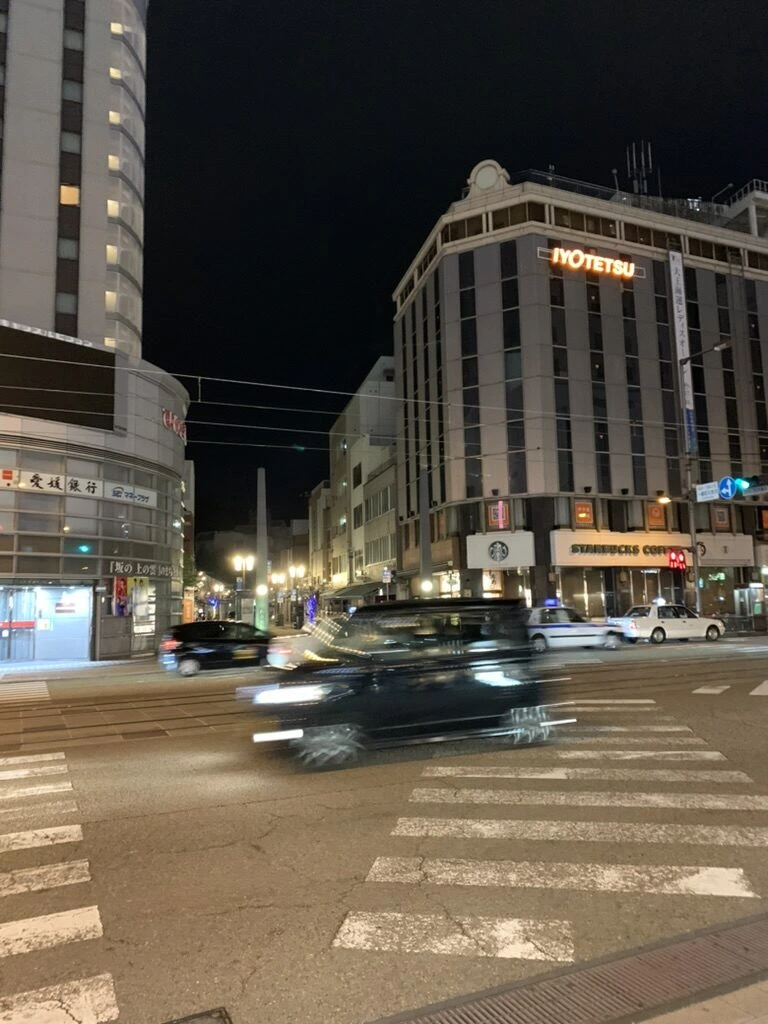 夜の大街道の交差点。左に円筒形の高い建物、右にIYOTETSUの看板のビル