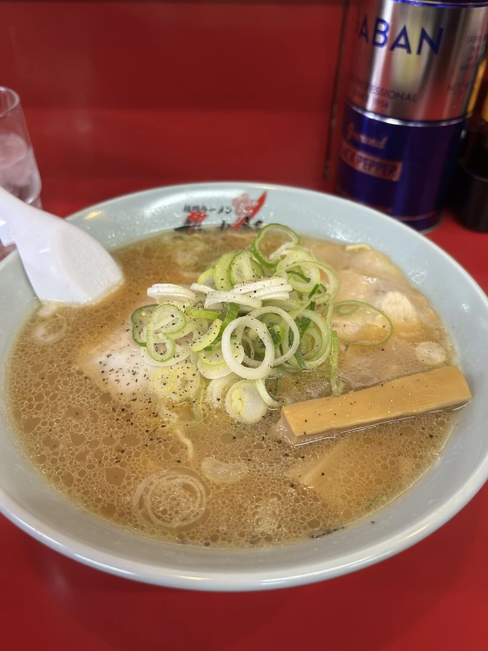 赤いカウンターに置かれた旭川ラーメン。薄茶色のスープに刻みねぎ、チャーシュー、メンマ