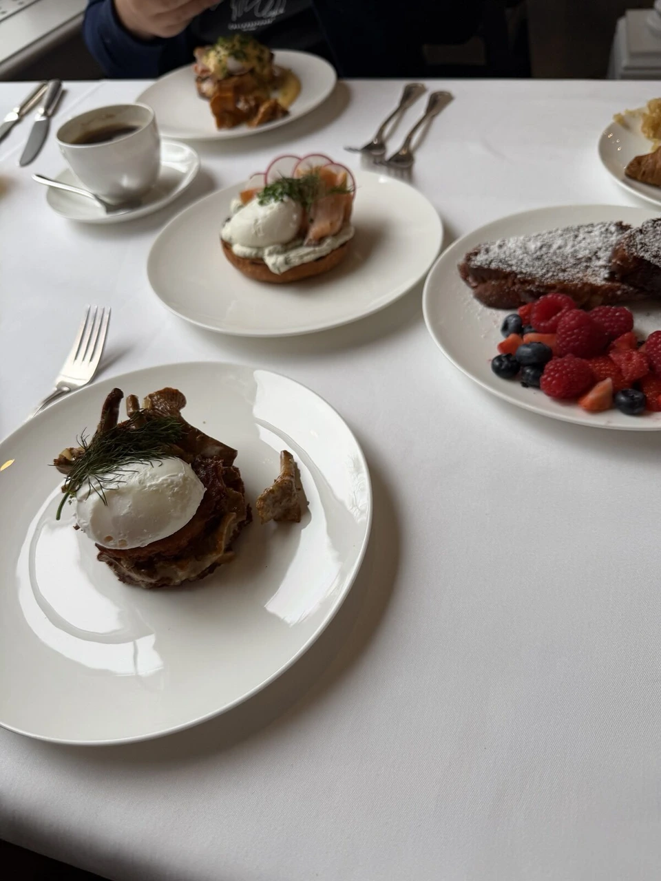 ホテル・ブリストルの朝食のテーブル。ポーチドエッグときのこの皿、サーモンとポーチドエッグのベーグル、ベリーをのせたフレンチトースト