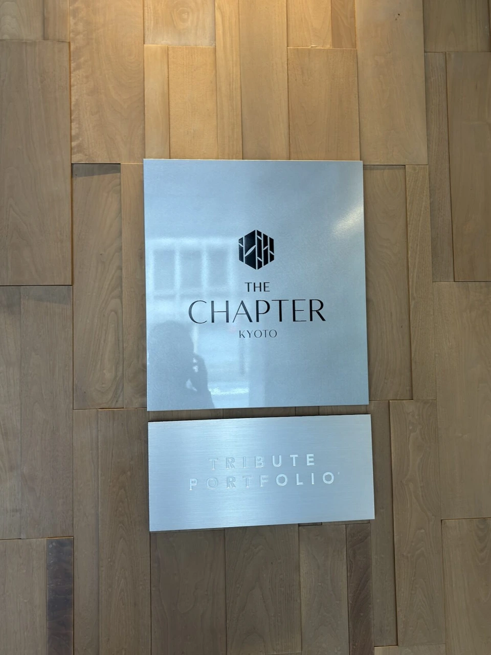 木の壁に掛けられた銀色のプレート。THE CHAPTER KYOTOとTRIBUTE PORTFOLIO