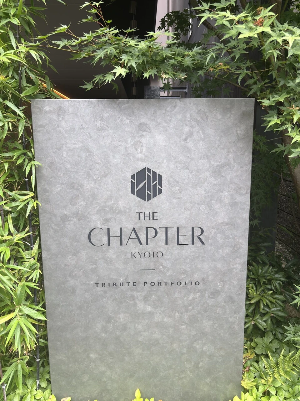 ザ・チャプター京都の植え込みの中に立つ灰色の石のサイン。THE CHAPTER KYOTO TRIBUTE PORTFOLIO