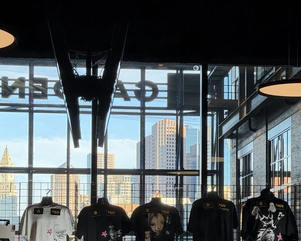 TDガーデンのグッズ売り場。黒いTシャツが並び、窓の外にカスタムハウスの時計塔