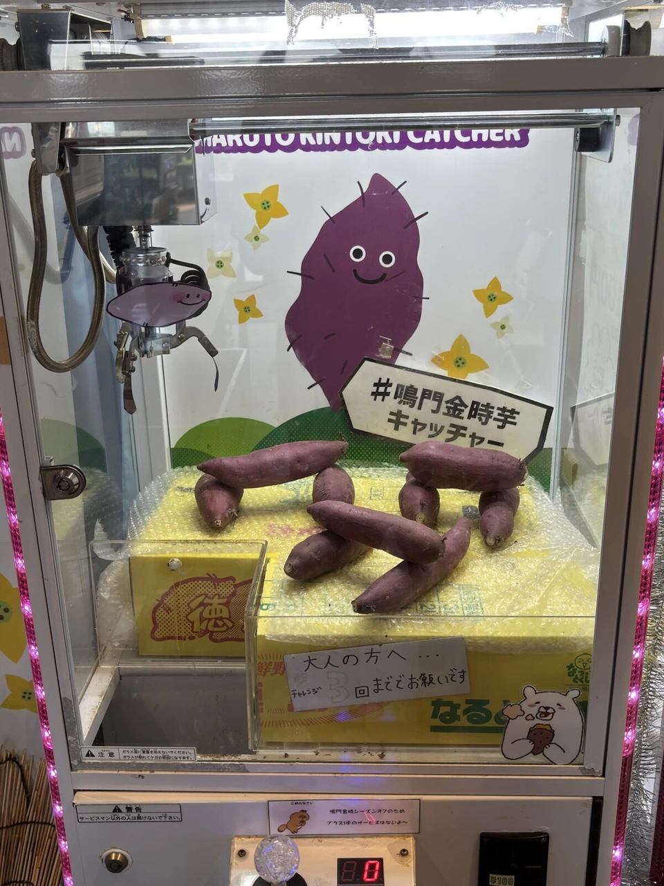 鳴門金時のさつまいもを景品にしたクレーンゲーム。紫色のさつまいもの絵の下に袋入りの芋が積まれている