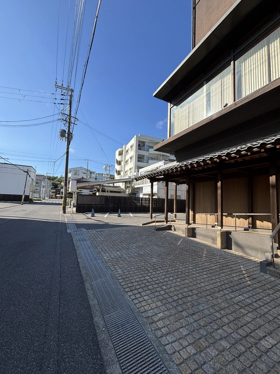 晴れた日の福良の町。石畳の歩道と瓦屋根の和風の建物、奥に白いマンション