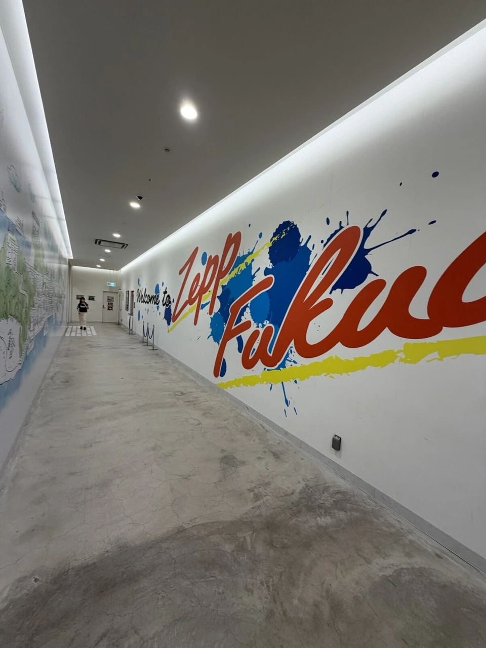 白い壁にカラフルな筆文字で描かれたFukuokaのアートがある通路