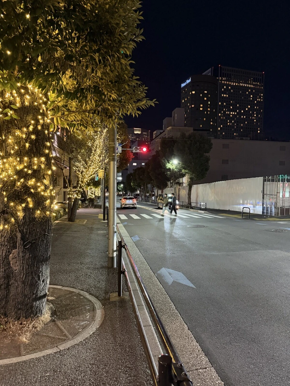 夜の高輪の坂道。街路樹に電飾が巻かれ、奥にホテルの高層棟