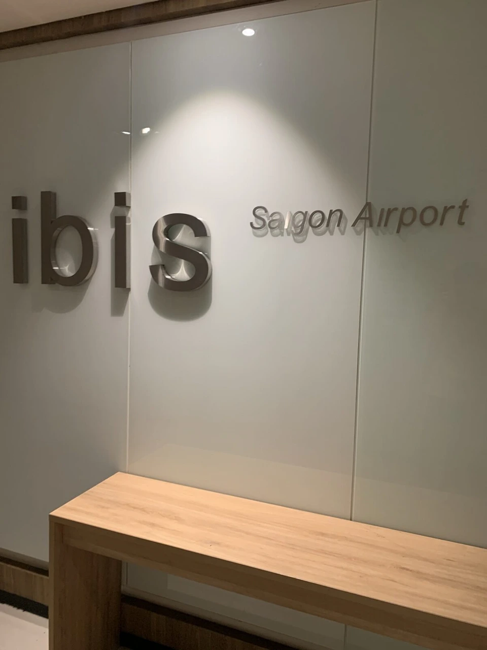 早朝のロビーの壁にあるibis Saigon Airportのロゴと木のベンチ
