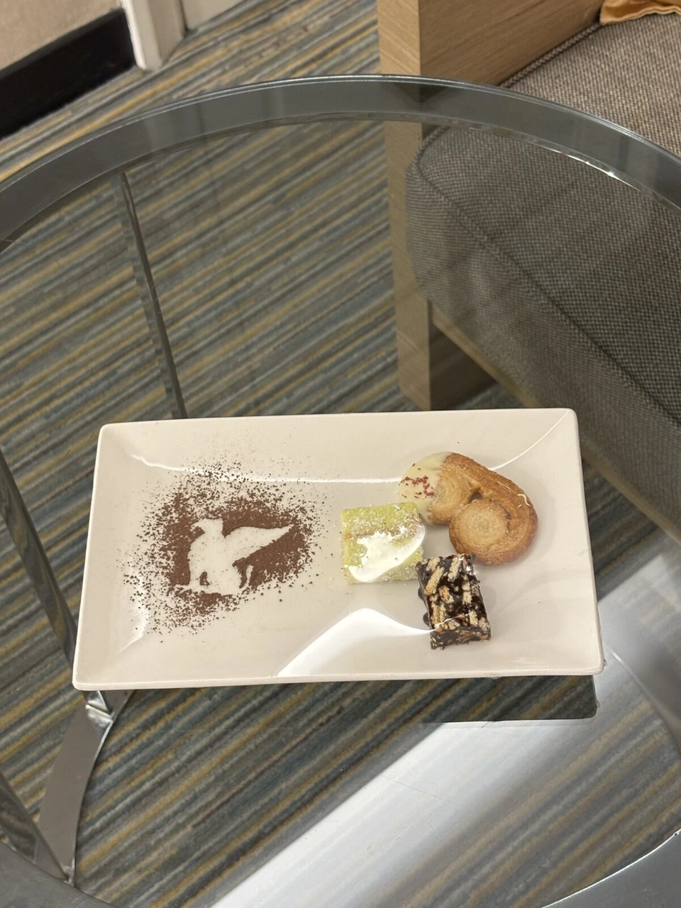ココアパウダーで鳥の絵が描かれた皿に、焼き菓子や小さなケーキ