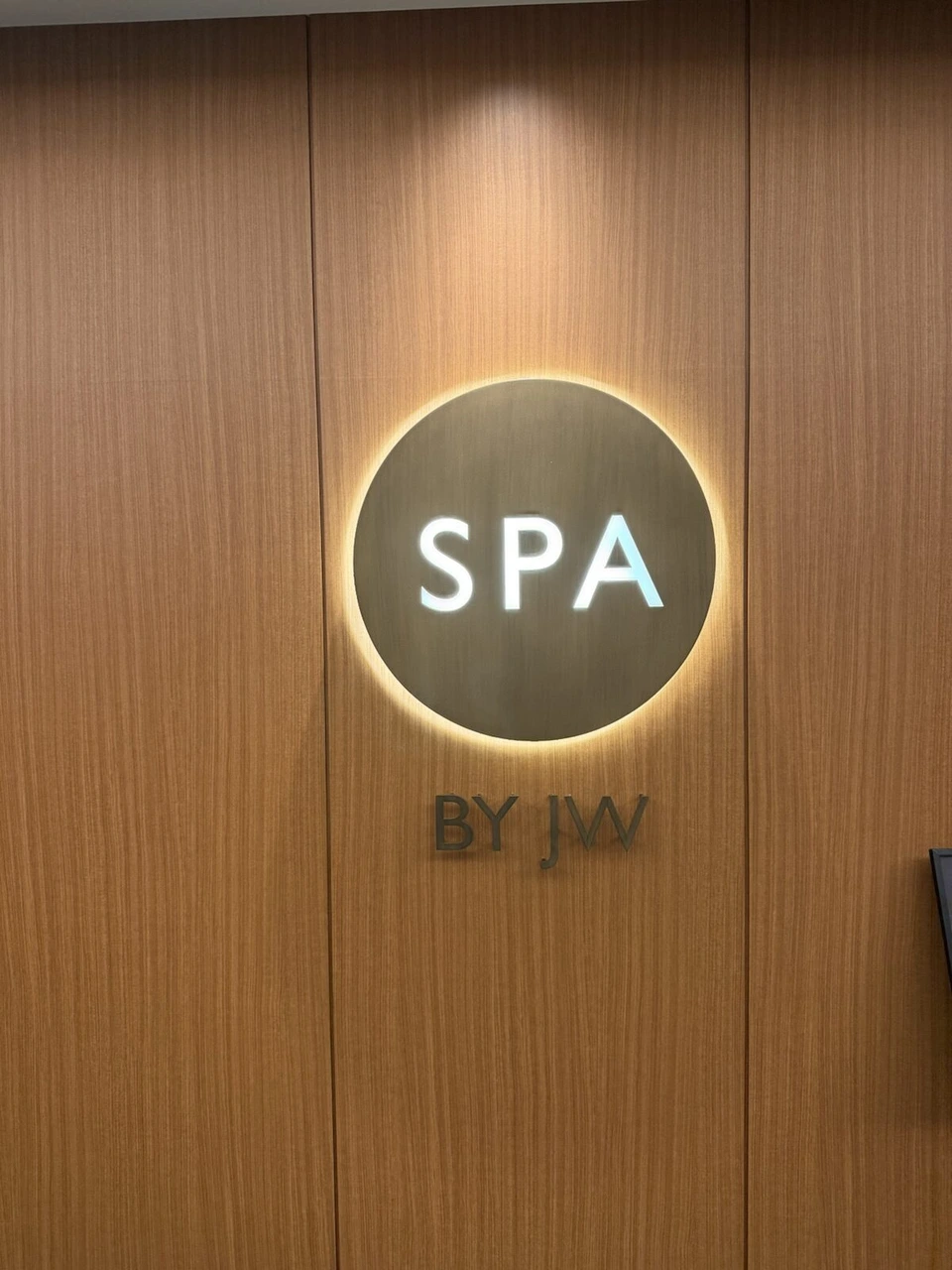 木目の壁に光るSPA BY JWの丸いサイン