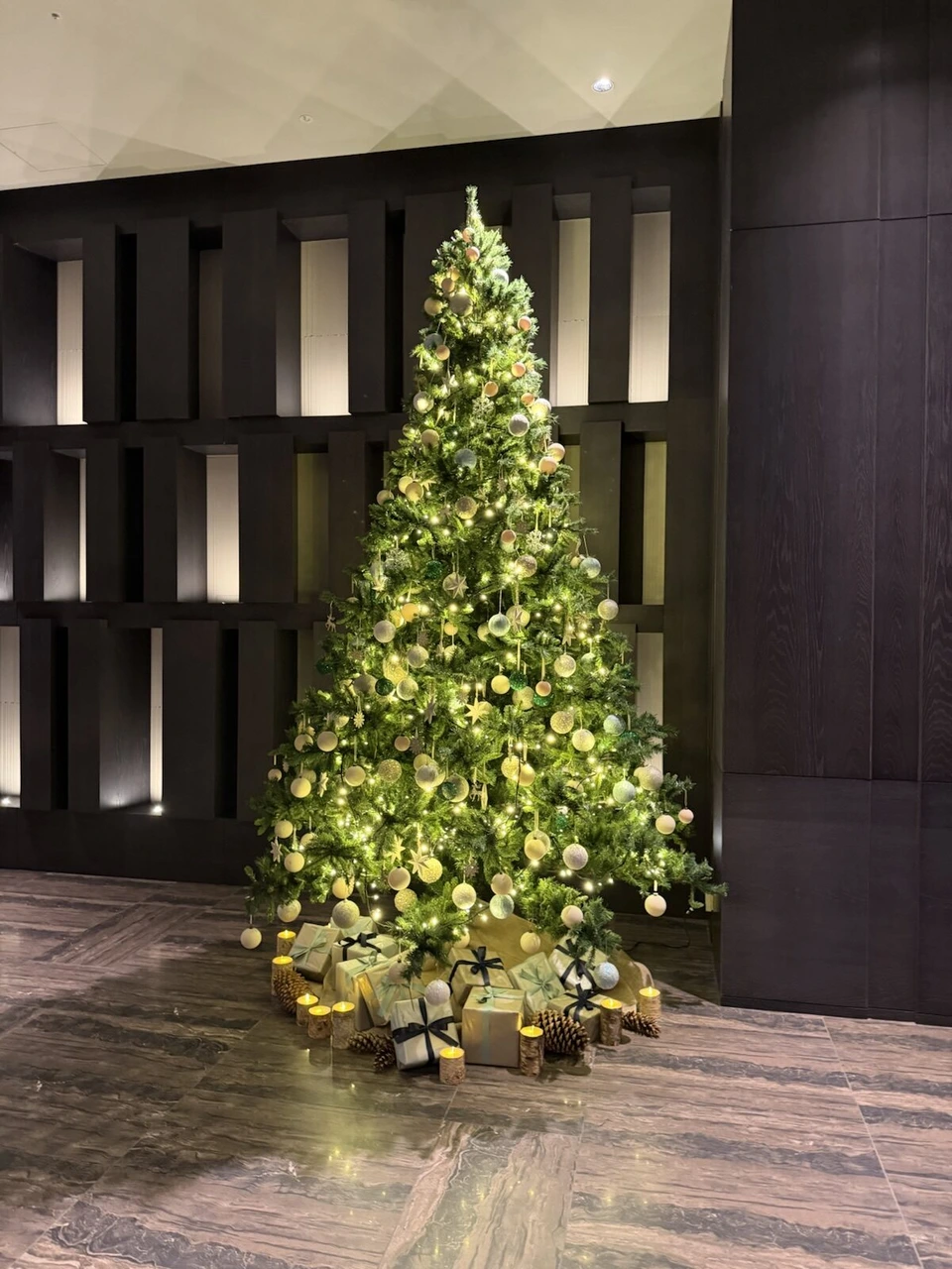 ロビーの黒い壁の前に飾られたクリスマスツリーとプレゼントの箱