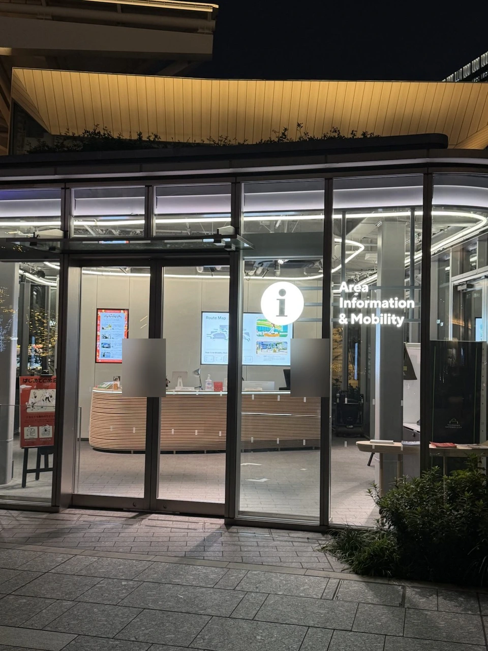 夜の高輪ゲートウェイシティの案内所。ガラス越しのカウンターとArea Information & Mobilityの表示