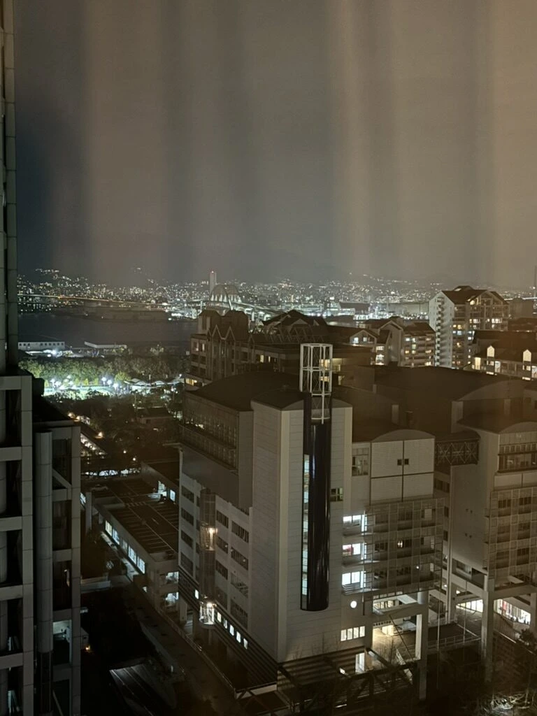 夕暮れの窓から見た六甲アイランドの建物と遠くの街の明かり