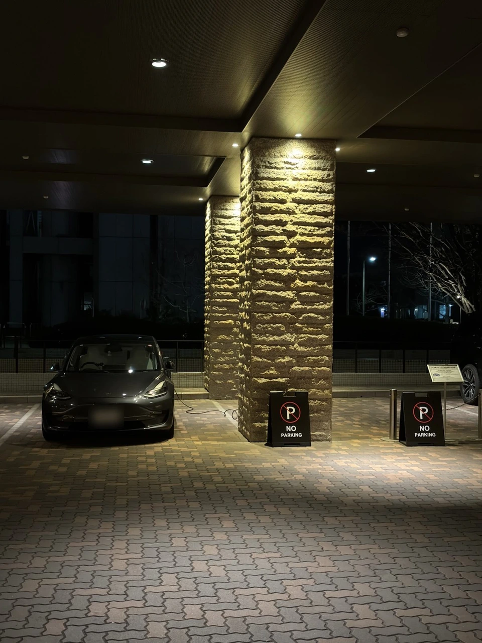 神戸ベイシェラトンの入口前の屋根の下に停めたテスラ。石張りの柱の横から充電ケーブルがのびている