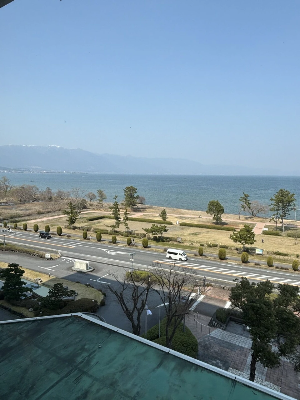 琵琶湖マリオットホテルの和室の窓から見た湖岸の公園と道路、その先の琵琶湖と対岸の山