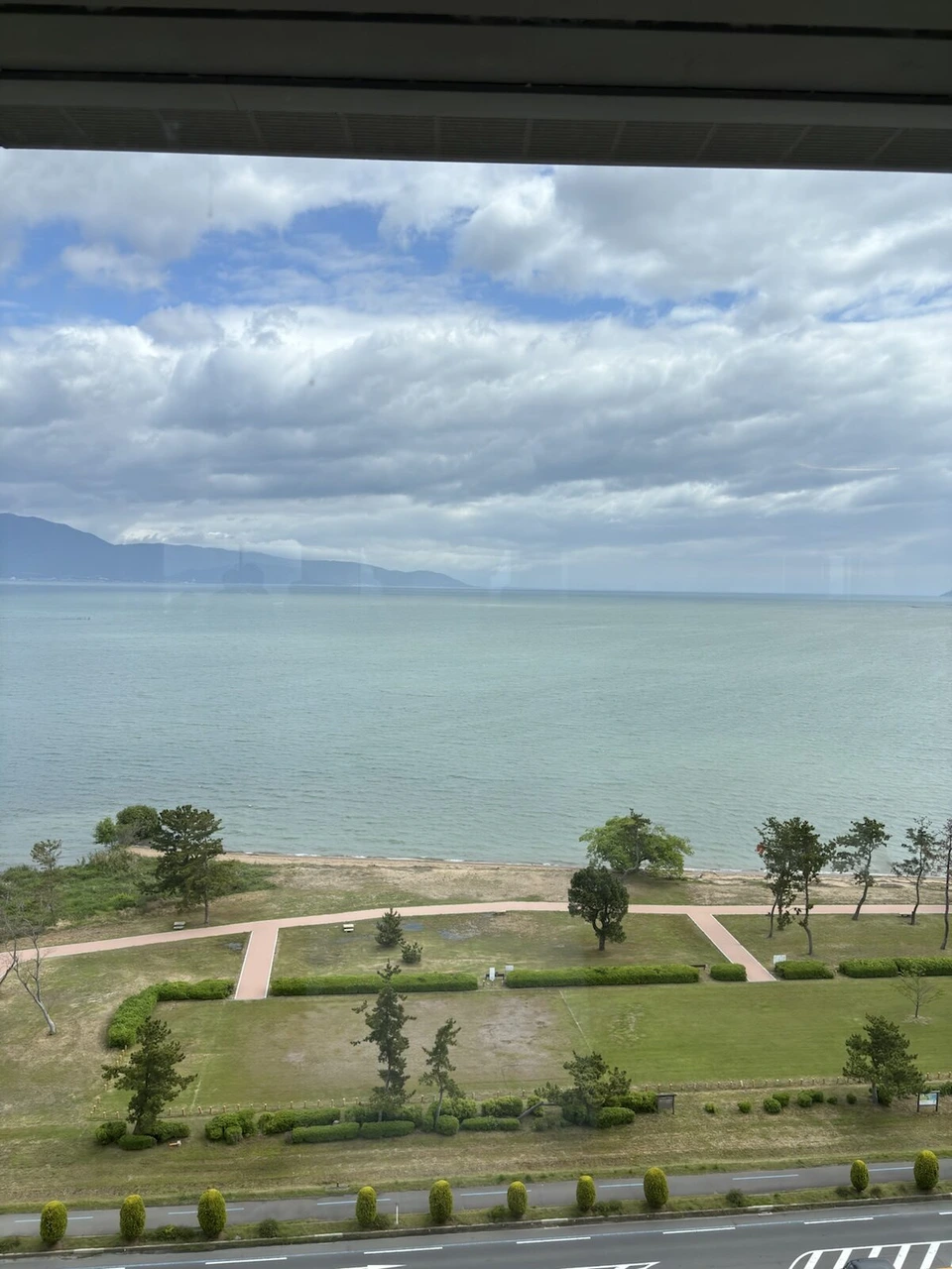 朝の琵琶湖マリオットホテルの客室の窓から見た湖岸の公園と琵琶湖、対岸の山