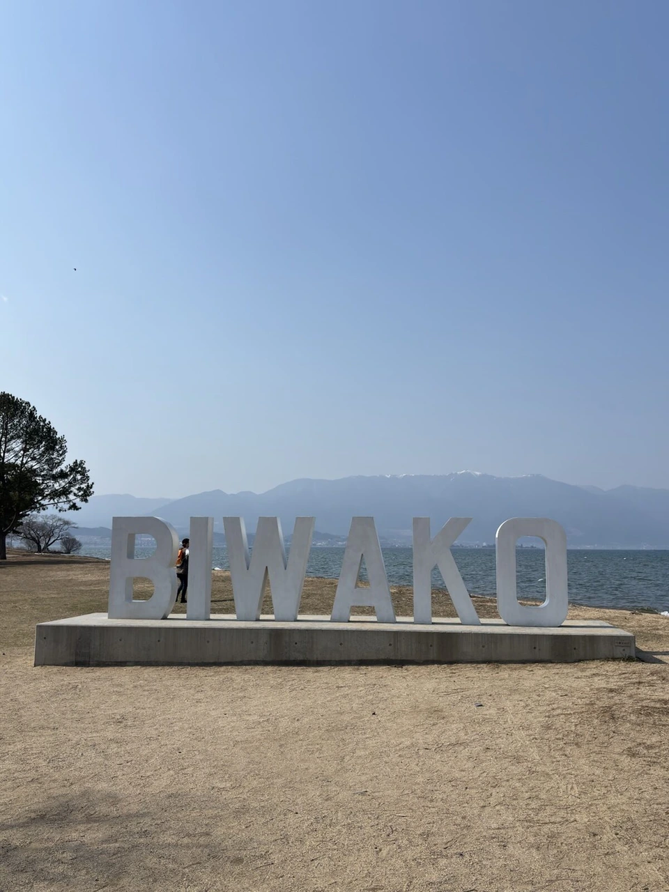琵琶湖マリオットホテルの前の湖岸の砂浜に立つBIWAKOの大きな文字のモニュメントと、青空と琵琶湖