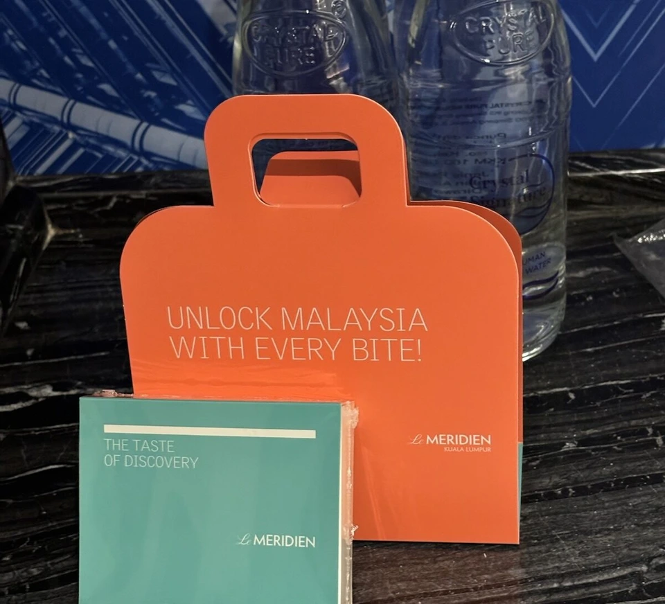 オレンジ色の手提げ型の箱UNLOCK MALAYSIA WITH EVERY BITE!と、緑色の小冊子THE TASTE OF DISCOVERY