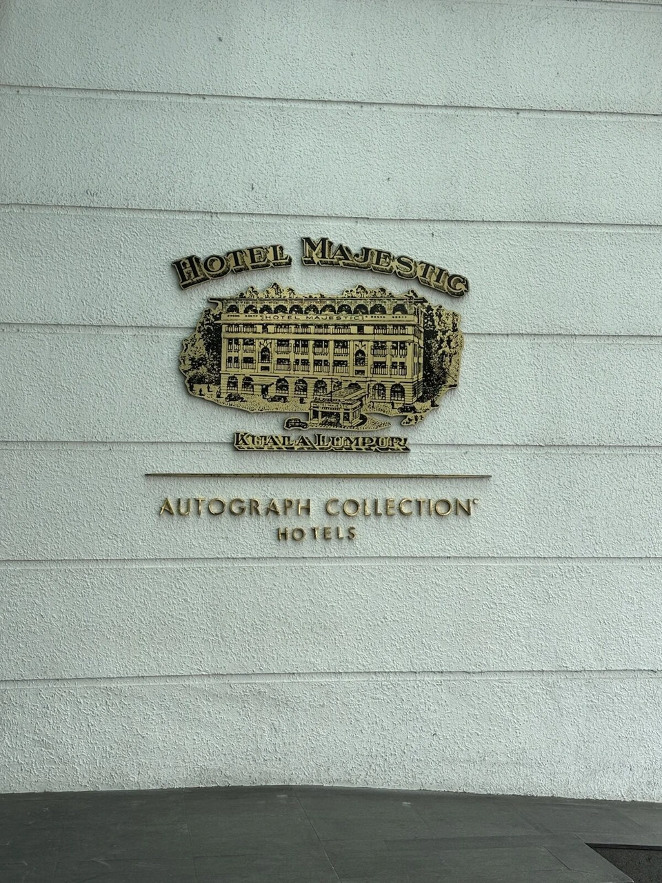 ザ・マジェスティック・ホテル・クアラルンプールの白い壁に付いたHOTEL MAJESTICの金色の建物レリーフとAUTOGRAPH COLLECTION HOTELSの文字