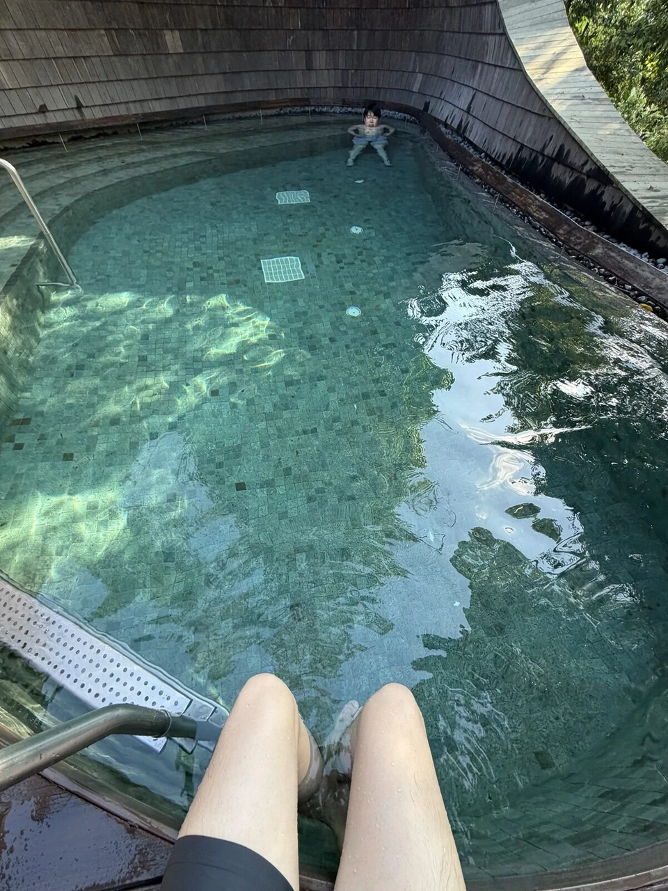 プールの縁に座って足を水につけた様子