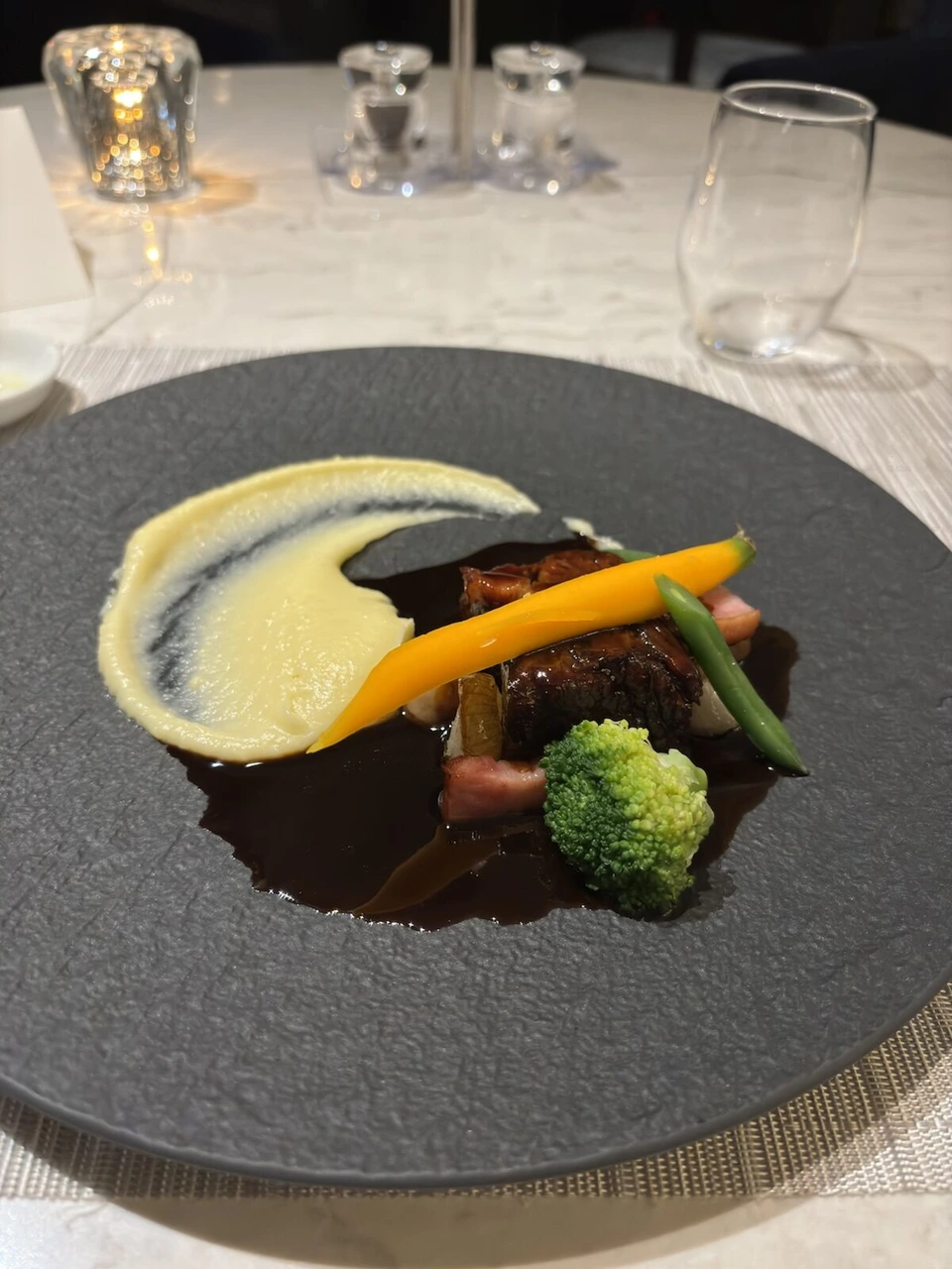 グレーの皿に盛られた肉料理。ピューレ、にんじん、インゲン添え