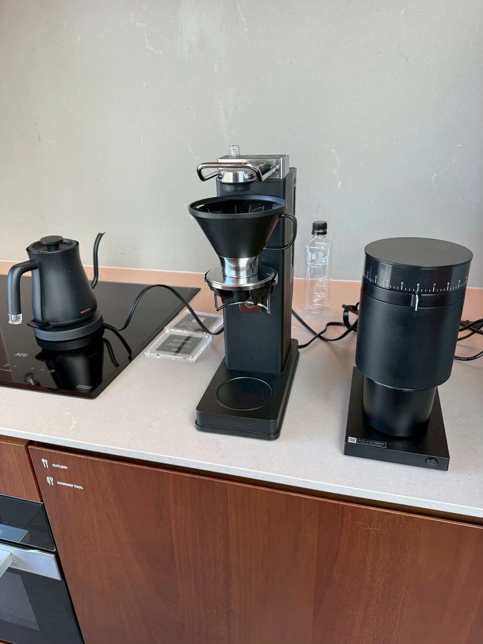 キッチンのカウンター。電気ケトルとコーヒーブリューワー、黒いコーヒーグラインダーが並ぶ