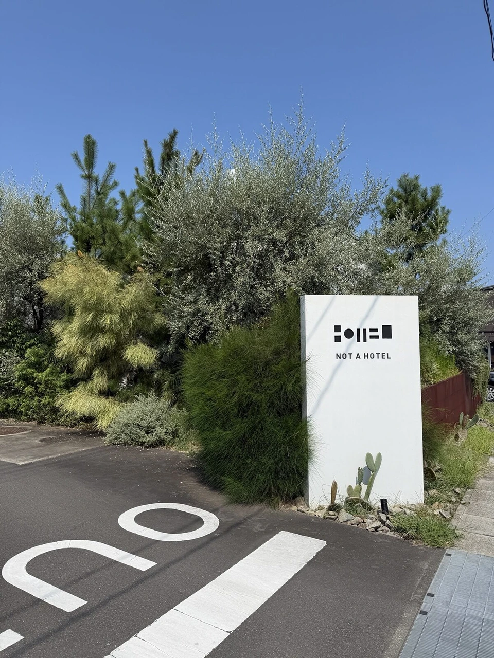 NOT A HOTELのロゴが入った白い看板と、駐車場の路面に書かれたINの文字