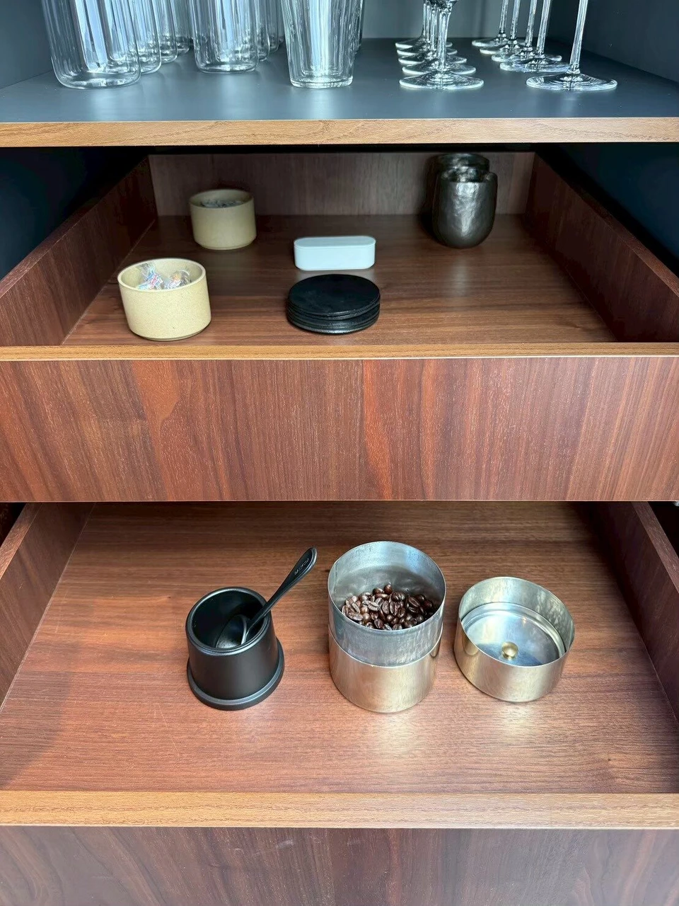 キッチンの棚。上段にグラス、引き出しに缶入りのコーヒー豆と小さな容器