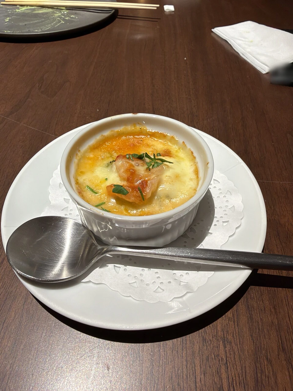 白い器に入ったグラタン。焼き色のついたチーズの上にエビとハーブ