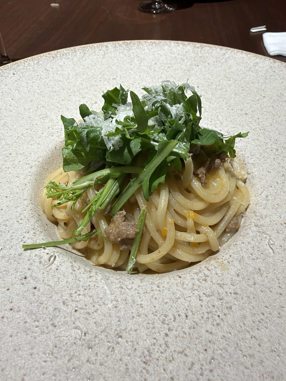 ざらっとした白い皿に盛られたパスタ。上に緑の葉とチーズ