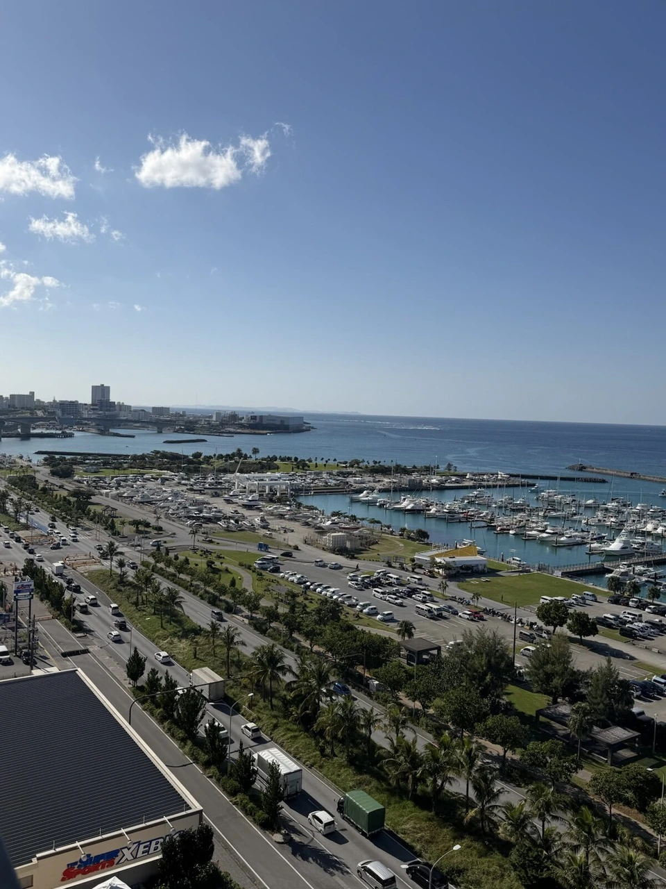 11階から南側を見た景色。宜野湾港マリーナに並ぶヨットと海沿いの道路、遠くに浦添・那覇方面の街