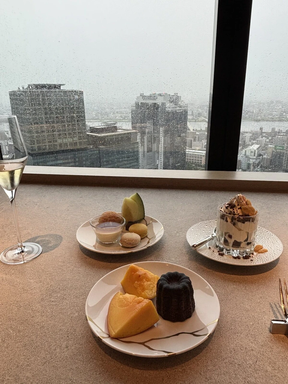 大阪ステーションホテルの窓際の席に並んだスコーン、カヌレ、パフェなどの軽食