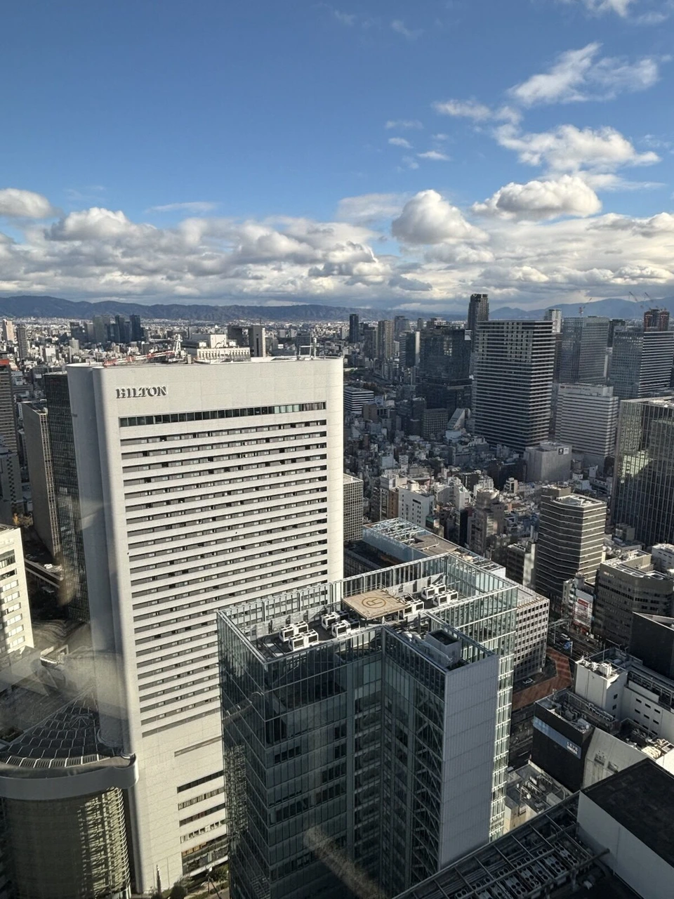 大阪ステーションホテルのシグネチャーツインの窓から見た昼の梅田の高層ビル群と青空