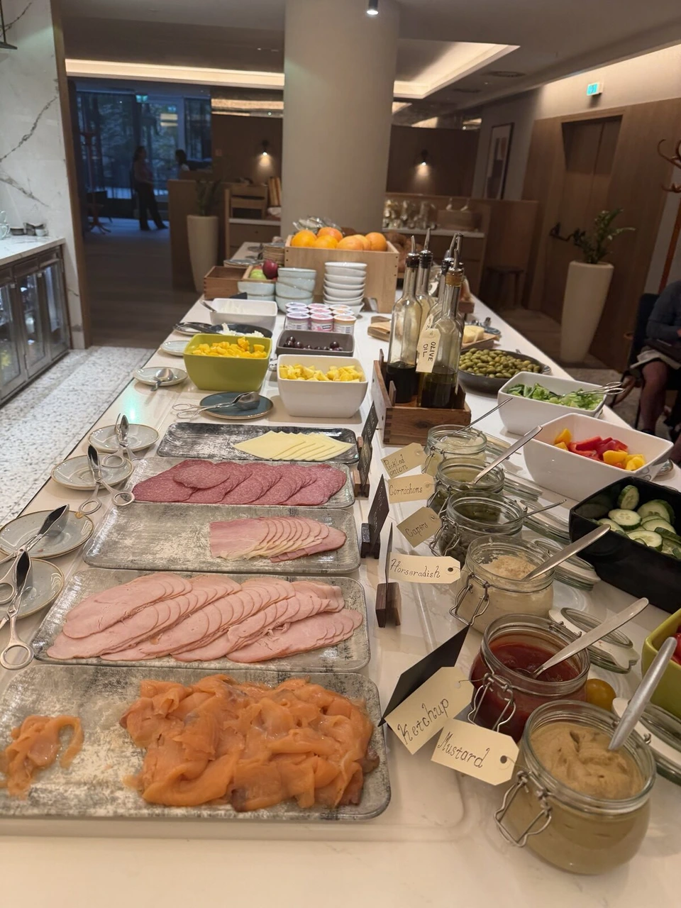 M Clubの朝食ビュッフェ。ハム、スモークサーモン、チーズ、ジャムの瓶が長いカウンターに並ぶ