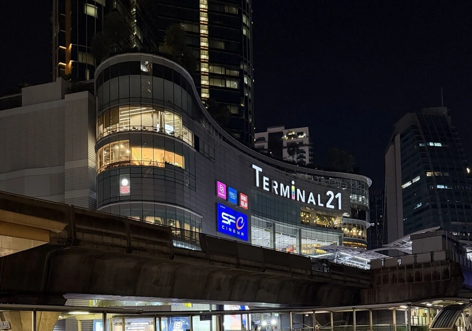 夜のターミナル21。曲線のガラスの建物にTERMINAL21の文字と映画館の看板、手前にBTSの高架と歩道橋