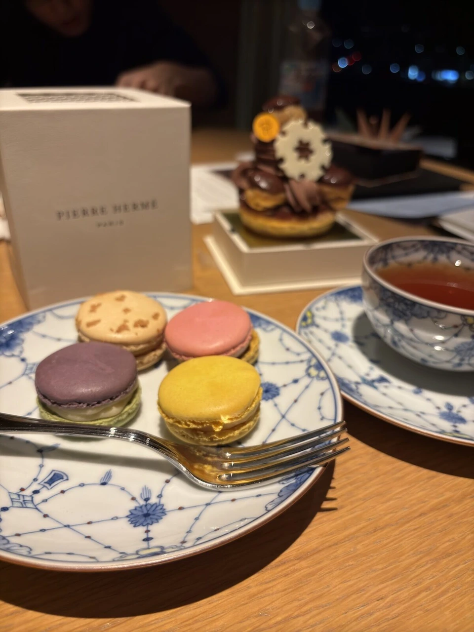 ブルーの柄の皿にのったマカロン4つと紅茶、奥にピエール・エルメの箱