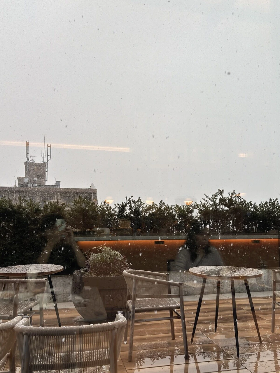 雪が舞うレストランのテラス席。テーブルと椅子、植栽
