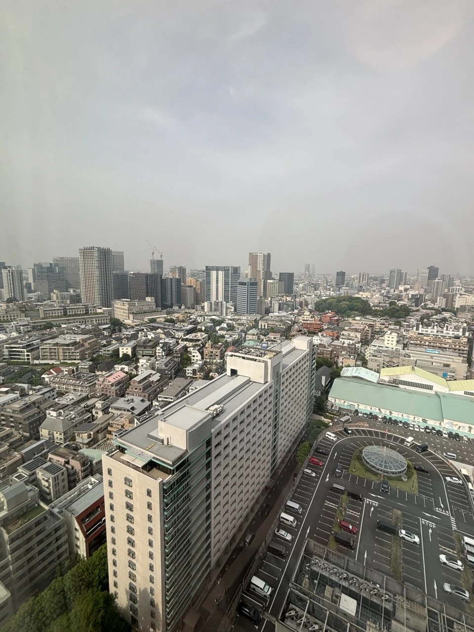 曇り空の朝、高層階の窓から見下ろした品川の街並み。手前に白いマンションと駐車場