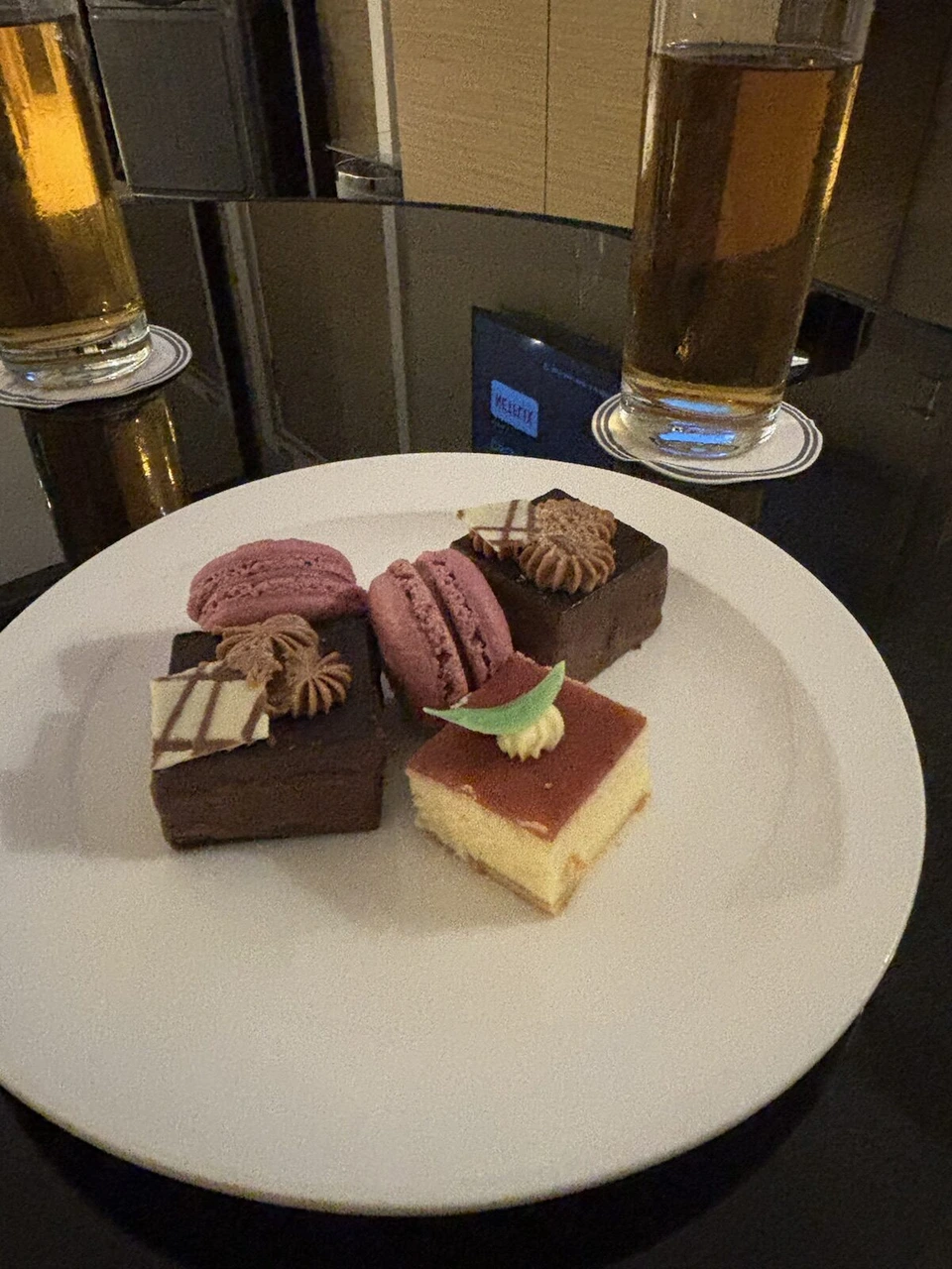 白い皿に盛られたマカロンやチョコレートケーキなど小さなケーキと、ビールのグラス