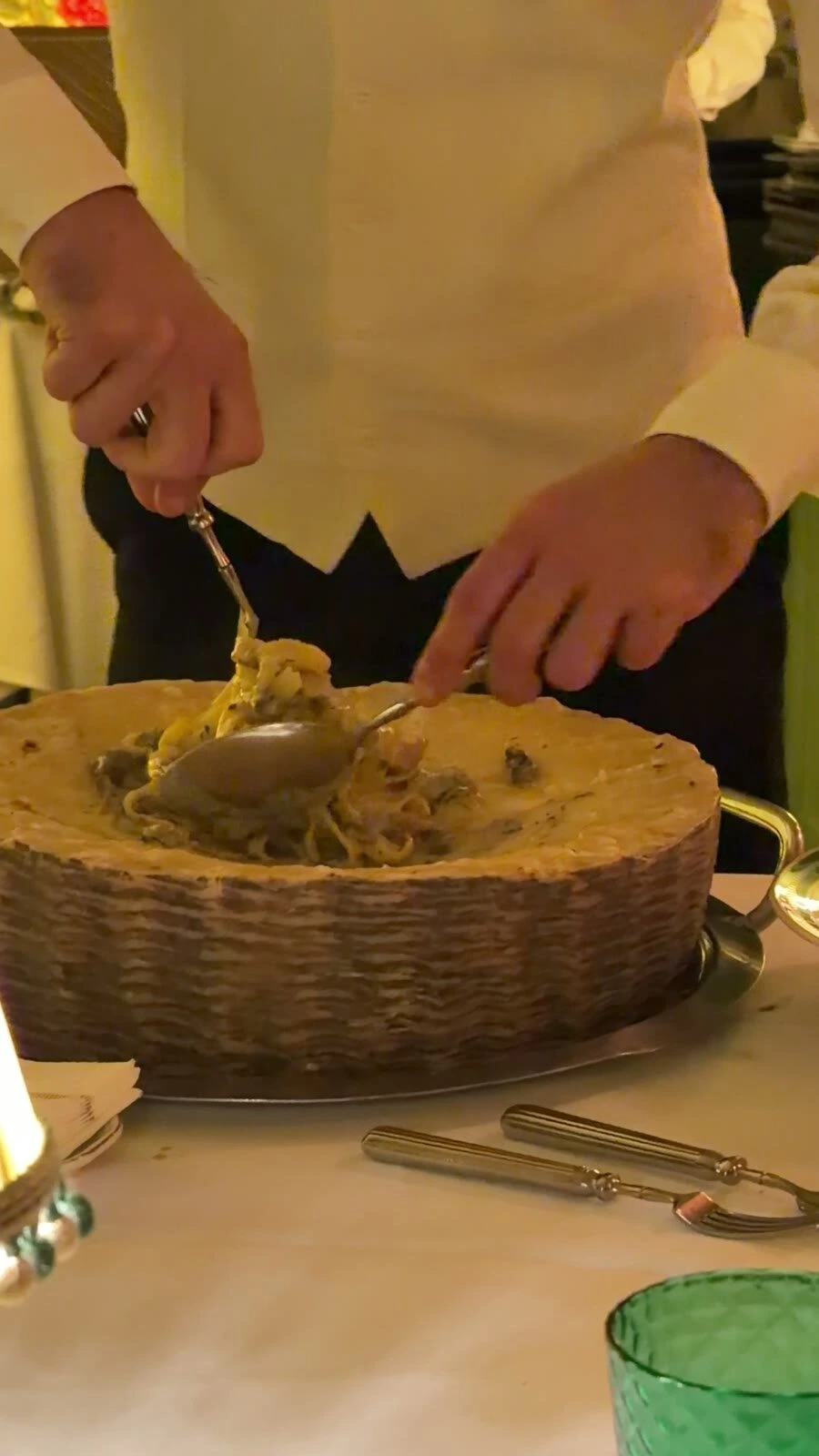 テーブルの横で、大きなチーズの塊の中でパスタを和えているところ