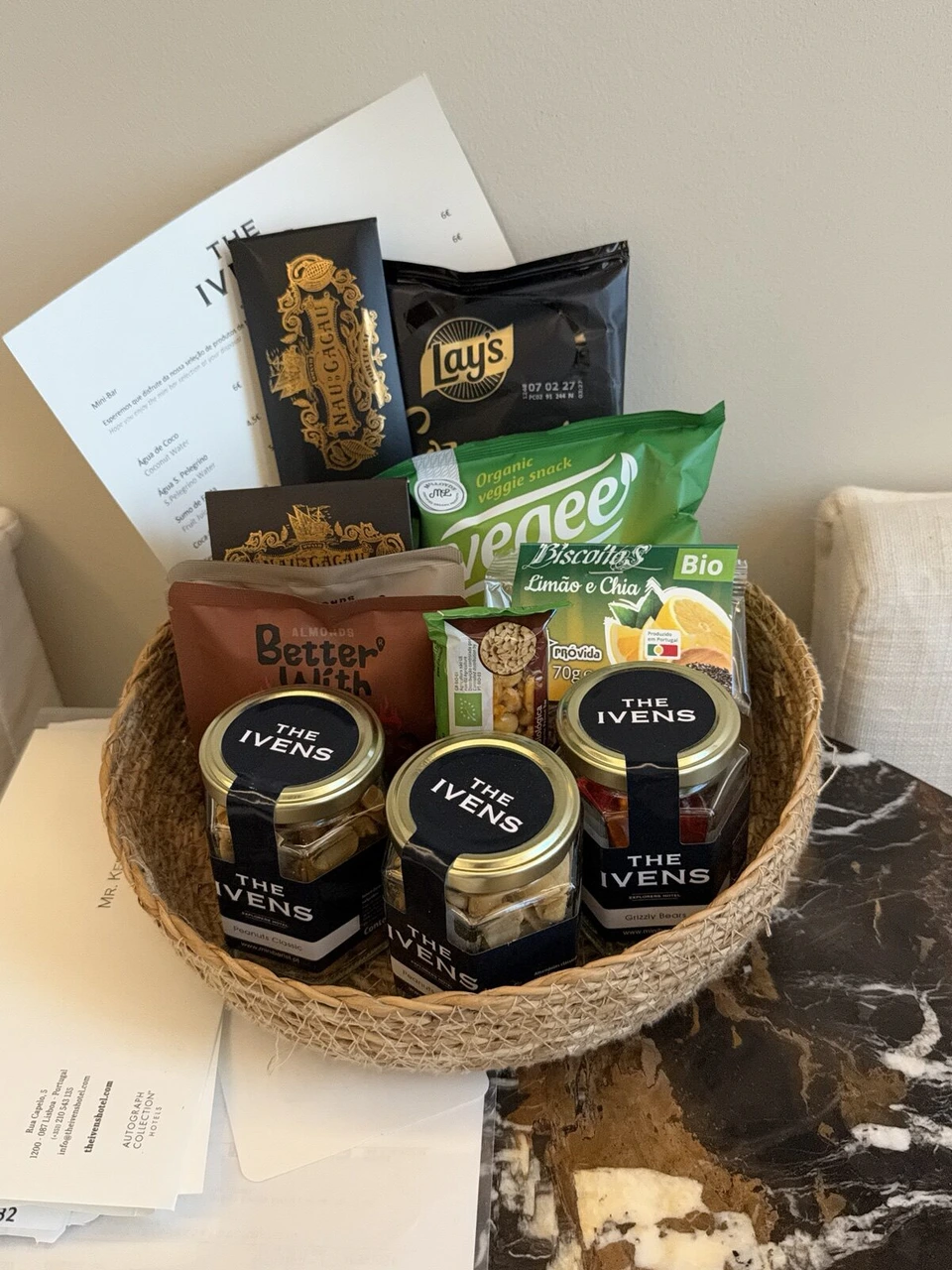 編みかごに入ったスナック。ポテトチップス、野菜チップス、チョコレート、THE IVENSのロゴ入りの小瓶のナッツ