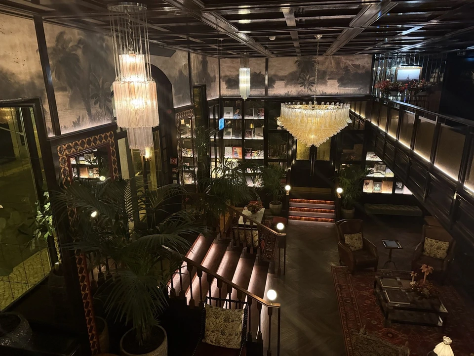 夜中のジ・アイヴェンスの館内。上の階から見た、シャンデリアの下がる吹き抜けと照明のともった階段、本棚