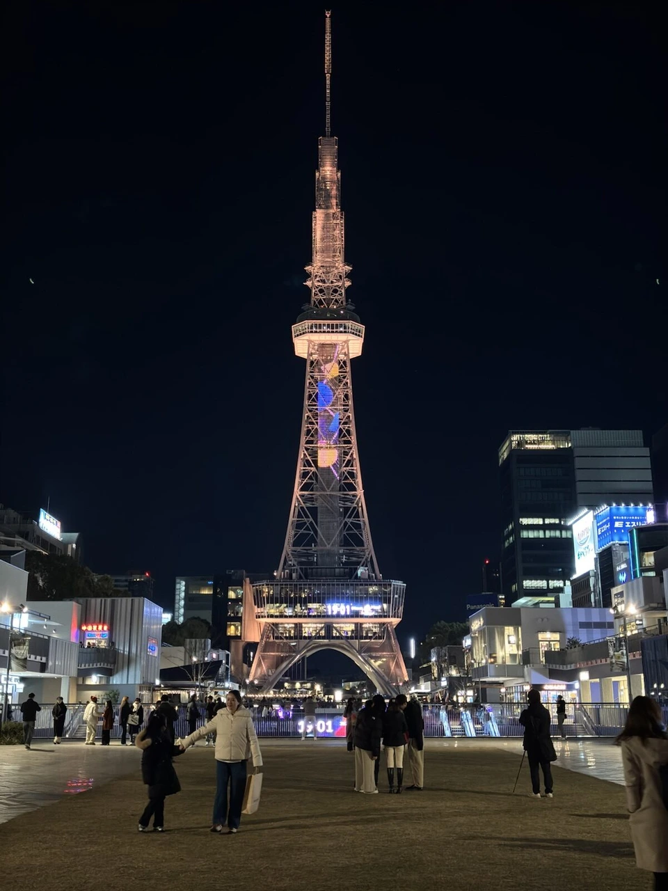 ライトアップされた中部電力 MIRAI TOWERと、芝生の広場を歩く人